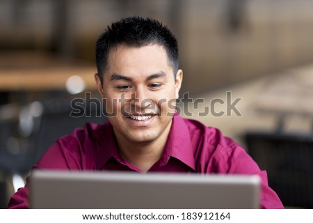 Stock photo of a well dressed Hispanic businessman looking down at a laptop while telecommuting from an internet cafe.