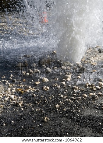Water from a broken water line bursts through the surface of the street, spreading rocky soil across the road.