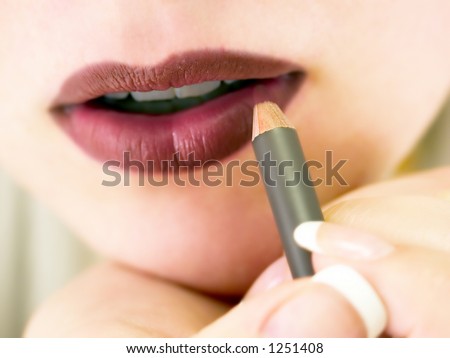 A closeup of a woman putting on lip liner.  Very slight motion blur on the hand and pencil.