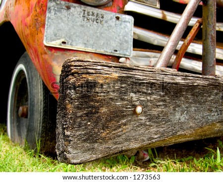 A wooden bumper on a beat up ,old, run down, rusting truck.  Medium DOF, sharp focus on the bumper.