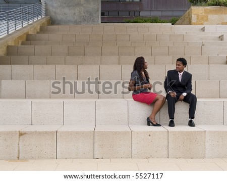 A businessman and businesswoman having a discussion while sitting in front of a modern building