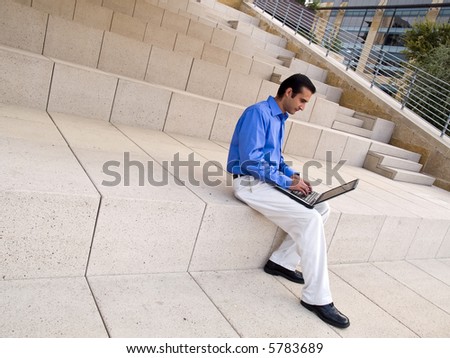 Handsome hispanic businessman surfing the internet on a laptop whle sitting on steps outside an office building.