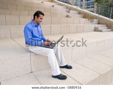 Handsome hispanic businessman surfing the internet on a laptop while sitting on steps outside an office building.