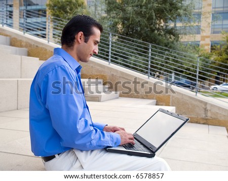 Handsome hispanic businessman surfing the internet on a laptop whle sitting on steps outside an office building.