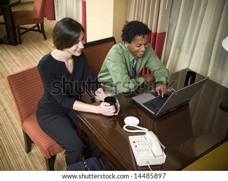 A business team cheerfully review good results on their laptop computer in a hotel room during a business trip.