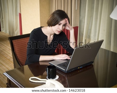 A businesswoman works late into the night on a frustrating problem using her laptop in her hotel room while on a business trip.