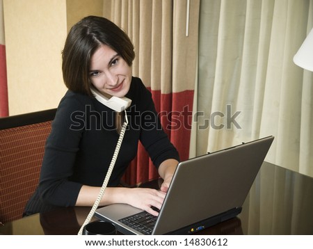 A businesswoman cheerfully reviews good results on her laptop computer in a hotel room during a business trip.