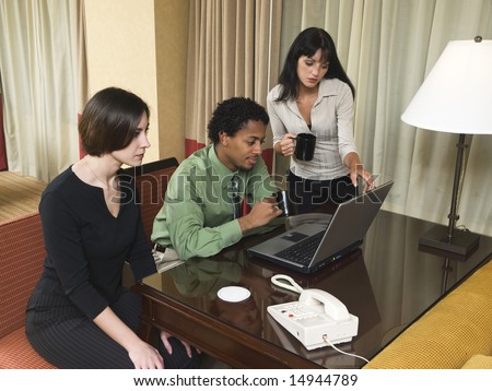 A team of businesspeople review results on a laptop while working late in a hotel room on a business trip.