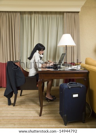 A businesswoman works late into the night on a laptop in her hotel room while on a business trip.