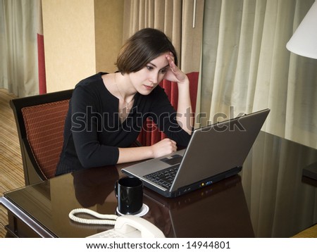 A businesswoman works late into the night on a frustrating problem using her laptop in her hotel room while on a business trip.