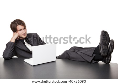 Isolated full length studio shot of a businessman kicking his heels up and working on his laptop while relaxing at a conference table.