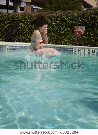 A beautiful young brunette woman in a bikini as she crashes into the pool with nose pinched and eyes closed.