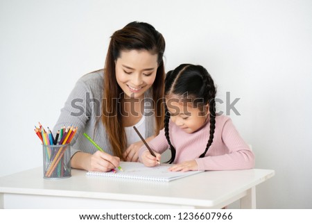 Asian moms are teaching crayon skills to Daughters. To draw a line. Write book on paper Artistic development Imagine And the mood of the children very well. And the family is very understanding love.
