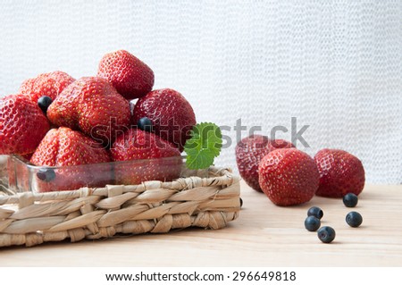 ripe strawberry garden and wild blueberries on a light background in a wicker basket