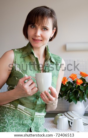 Cute housewife with cup of tea in kitchen after domestic work