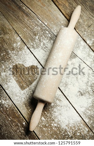 Heart Drawn In Sprinkled Cooking Flour. Wooden Rolling Pin With Remnants Of Flour In A Rustic Kitchen On An Old Grainy Textured Wood Surface