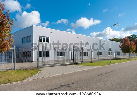 Modern Exterior Of An Industrial Building, Surrounded By A Fence With Iron Gate