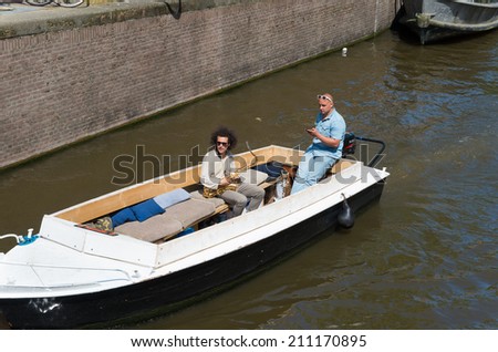 AMSTERDAM - MAY 18, 2014: Two unknown musicians in a boat on an amsterdam canal. Amsterdam counts 165 canals with a total length of 100 km.