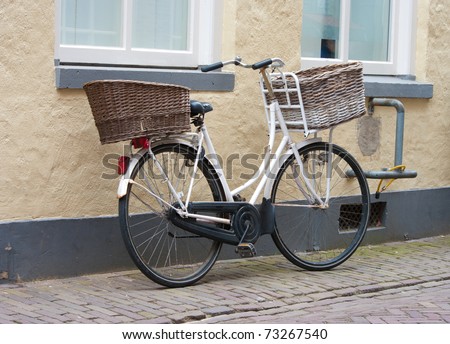 ladies bike with two reed baskets parked against a wall