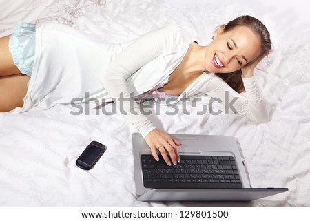 young happy woman on the bed with laptop and mobile phone