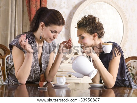 Two girl-friends talk and drink tea in drawing room