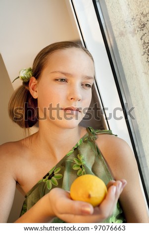 beautiful girl with green eyes is near the window and holds lemon,focus on left eye (close to window)
