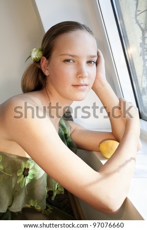 beautiful girl with green eyes is near the window and holds lemon