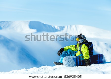 Vertical full length shot of a female snowboarder wearing yellow pants blue jacket yellow helmet and ski goggles posing with her snowboard at the mountains extreme sports recreation free ride concept