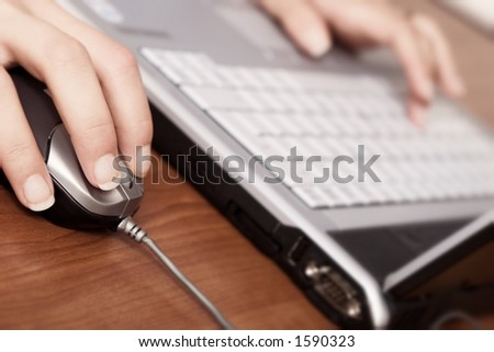 Young woman working on a laptop, close-up on the hand and mouse