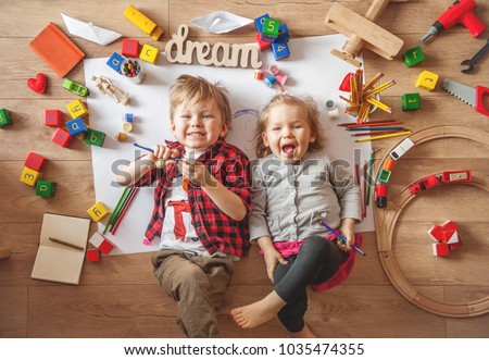 Kids drawing on floor on paper. Preschool boy and girl play on floor with educational toys - blocks, train, railroad, plane. Toys for preschool and kindergarten. Children at home or daycare. Top view