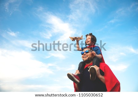 Father and son playing in aviator. Superman dad and son having fun. Imagination and dreams of being a pilot. Child pilot with airplane on dads back. Travel and vacation in summer. Freedom