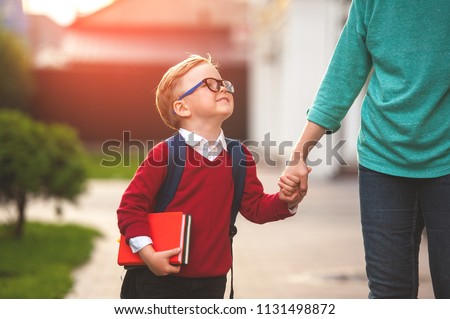 Parent take child to school. Pupil of primary school go study with backpack outdoors. Mother and son go hand in hand. Beginning of lessons. Back to school. First day of fall. Elementary student.