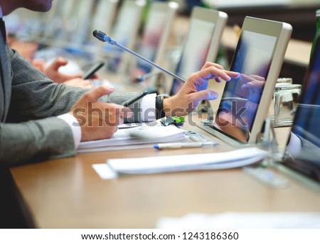 Conference room or seminar meeting room in business event. Session of Government. Business man finger touching screen on tablet pc. working in modern bright office while type your text