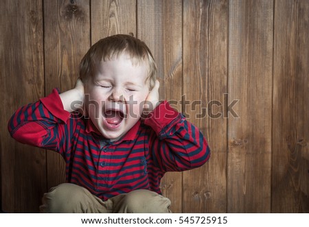 Cute boy shouts covered his ears with his hands. Stressed child. boy shouting on wooden background. Space for text. sad and unhappy child. Upset toddler boy. problem child with head in hands