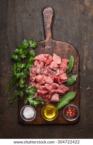raw ingredients for stew. pork meat cubes, oil ,salt and fresh seasoning on old rustic cutting board on dark wooden background top view