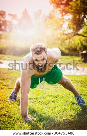 Sports man with brown hair and a beard on a natural background, performing push-ups on one arm