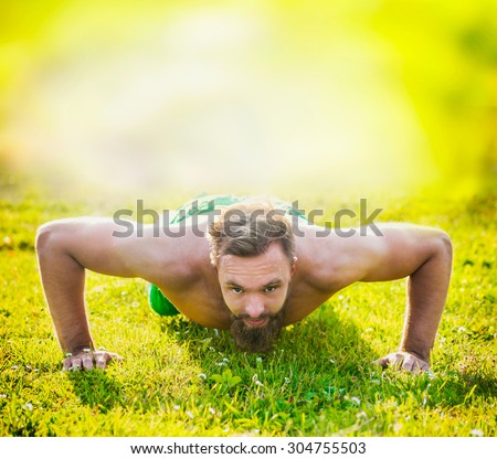 Sports man with brown hair and a beard on a natural background, performing push-ups