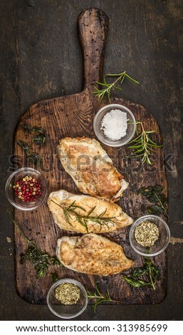 Spicy baked chicken breast on rustic wooden gutting board, top view