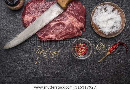 ingredients for cooking raw beef steak with salt and pepper carving knife pepper mill on a dark rustic background top view horizontal