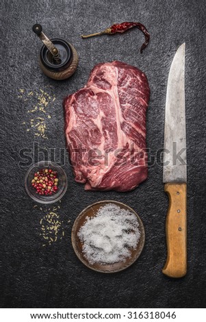 ingredients for cooking beef steak with salt and pepper  carving knife, pepper mill on a dark rustic background top view