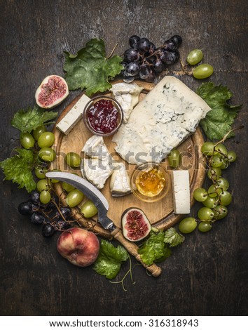 cheese plate with gorgonzola and Camembert cheese with Knife for cheese  white and dark grapes, honey and jam on a wooden cutting board on a dark rustic background top view close up