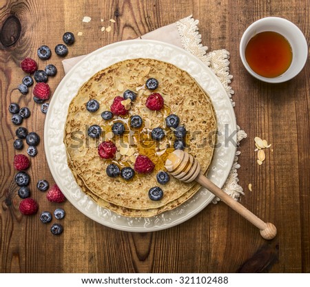 delicious pancakes with fresh berries with honey, almonds cup of tea with honey spoon on white plate with napkin on wooden rustic background top view