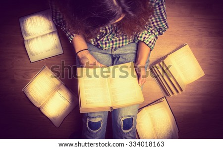 girl in a shirt holding a book sitting on the floor around her spread open books close up  retro  toning