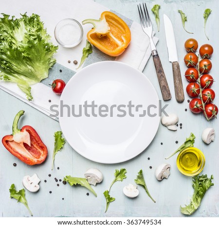 Ingredients for cooking salad cherry tomatoes, lettuce, peppers, spices and oil  laid out around a white plate on wooden rustic background top view close up