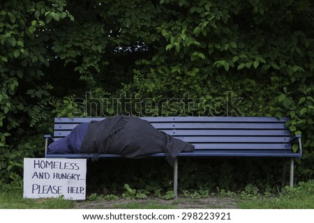 Homeless man on a park bench with a cardboard sign