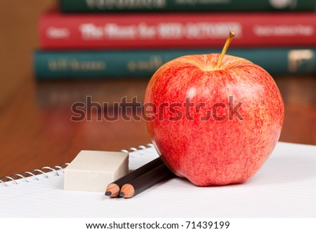 apple, pencil and eraser on top of a notebook with out of focus books in the background. afternoon snack sits on an open spiral notebook