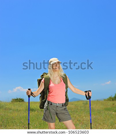 A smiling woman posing with backpack and hiking poles posing outdoor