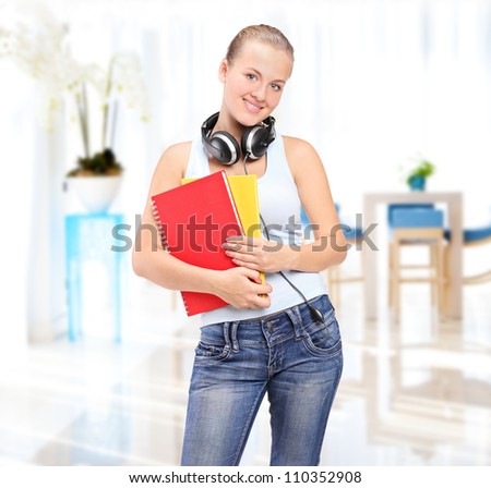 Female student with headphones holding books in a school hall