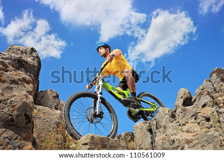 Person riding a mountain bike amid rocks on a sunny day against a blue sky and clouds, low angle view