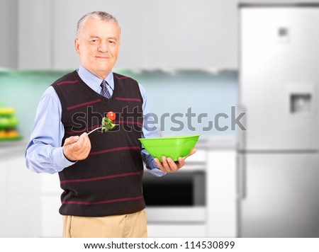 A mature man eating salad during a lunch, with kitchen in the background